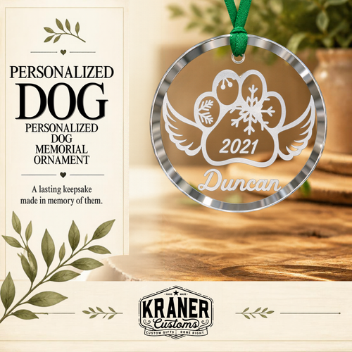 Personalized dog memorial ornament package by Kraner Customs, featuring a round clear glass ornament with a silver rim and a green hanging ribbon. The ornament is engraved with a dog silhouette, heart, snowflake, wings, the year 2021, and the name Duncan.
